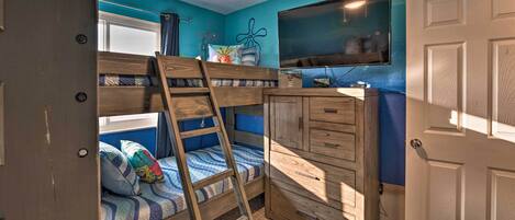 A bunk bed with a ladder, a wooden dresser, and a television on the wall.