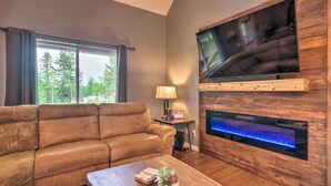 Uma sala de estar com sofá de couro, uma mesa de centro com um livro e uma planta, uma TV fixada em uma parede de madeira e uma lareira com um recurso aquático iluminado em azul.