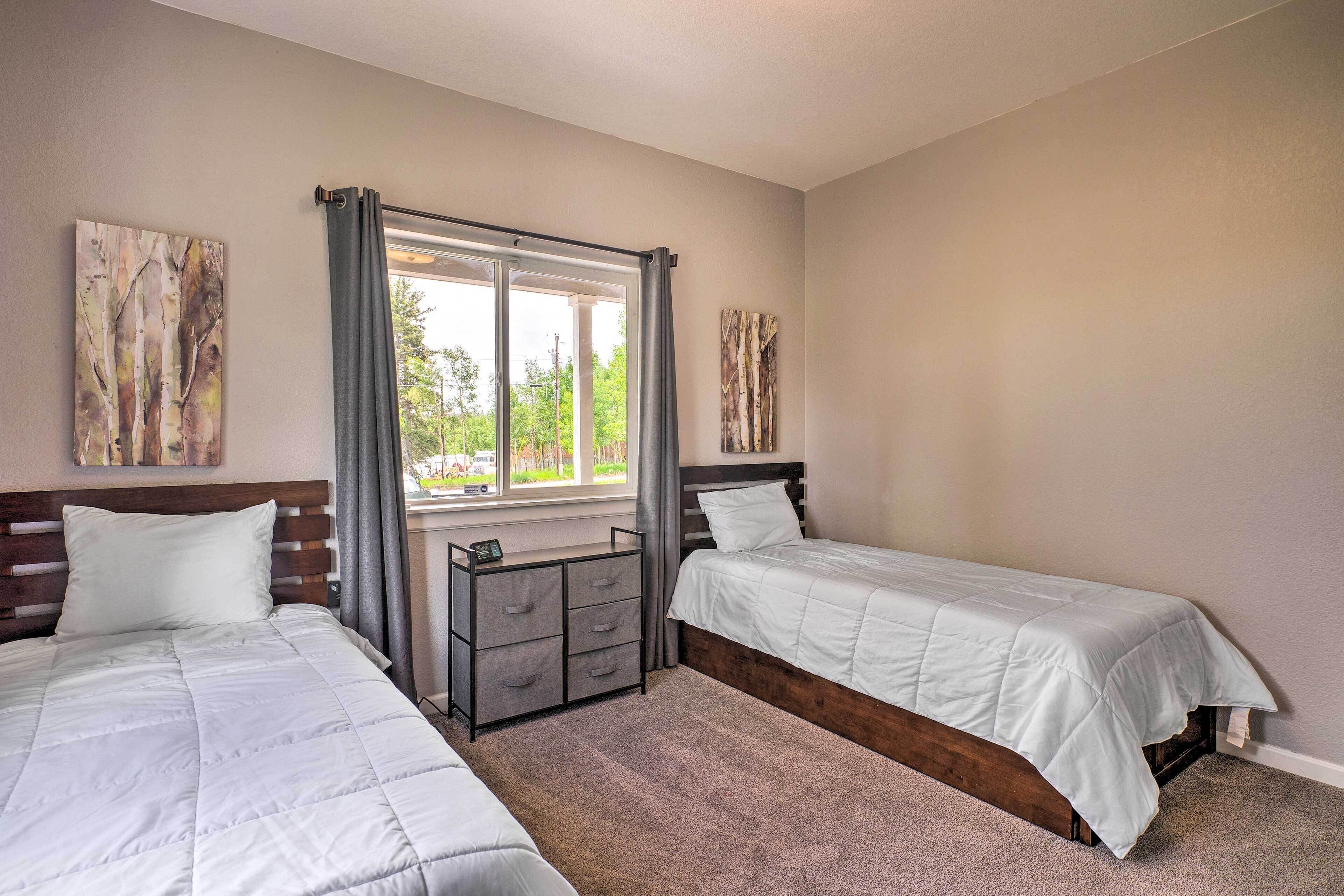 A bedroom with two beds, a window with curtains, and artwork on the walls.