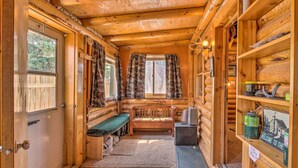 A log cabin interior with a bench, a small table, a door, and a shelf with a welcome sign.