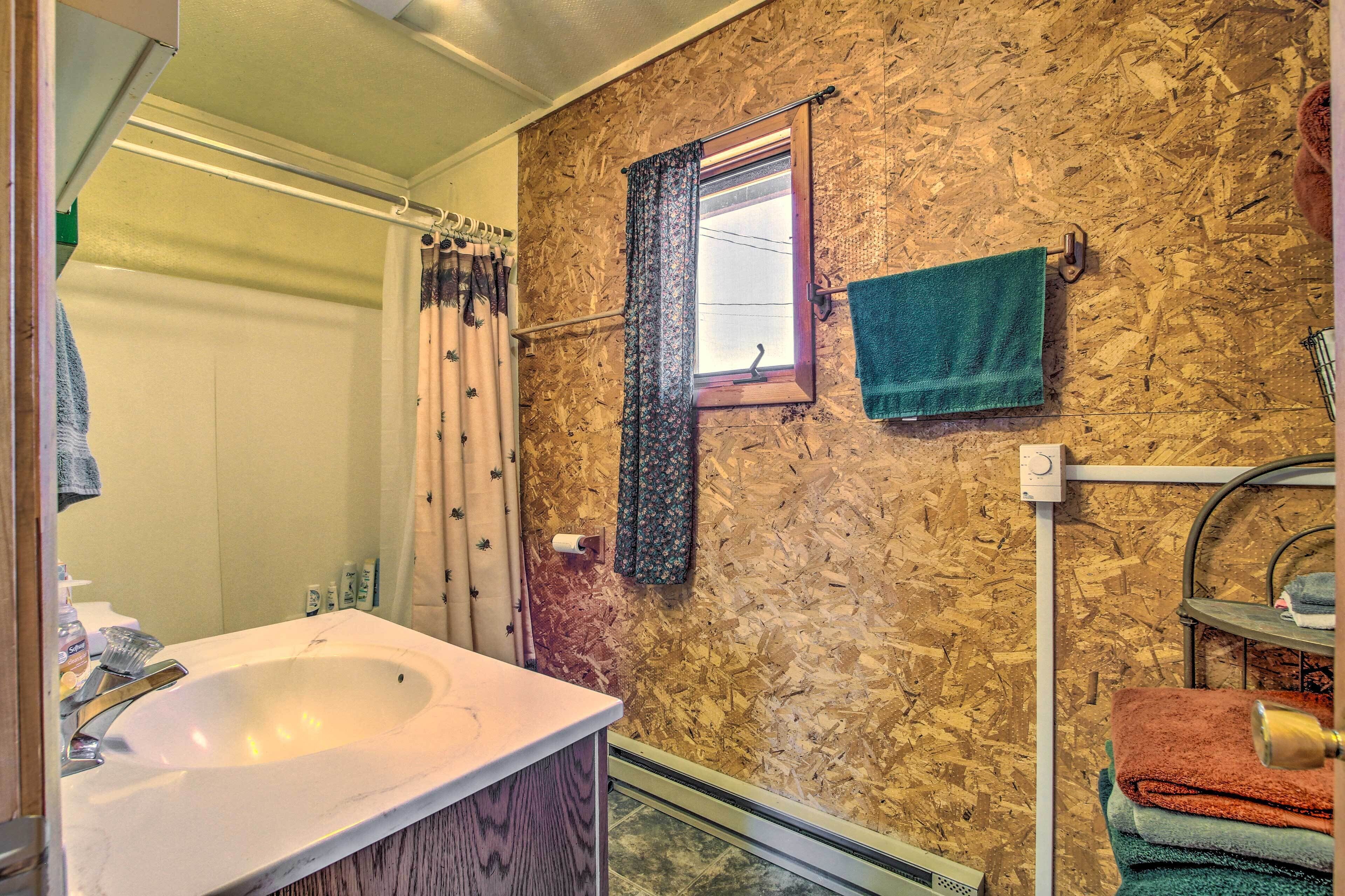 Een badkamer met een witte wasbak, houten lambrisering, een raam met gordijn en een handdoekrek met opgevouwen handdoeken.