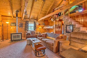 L’intérieur d’une cabane en rondins, avec un escalier en pierre, des meubles en bois, une cheminée et un téléviseur.