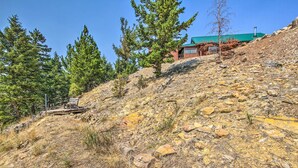 A cabin on a rocky hillside with a green roof, surrounded by pine trees.