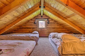 A cozy attic bedroom with two beds, a small window, and wooden beams.