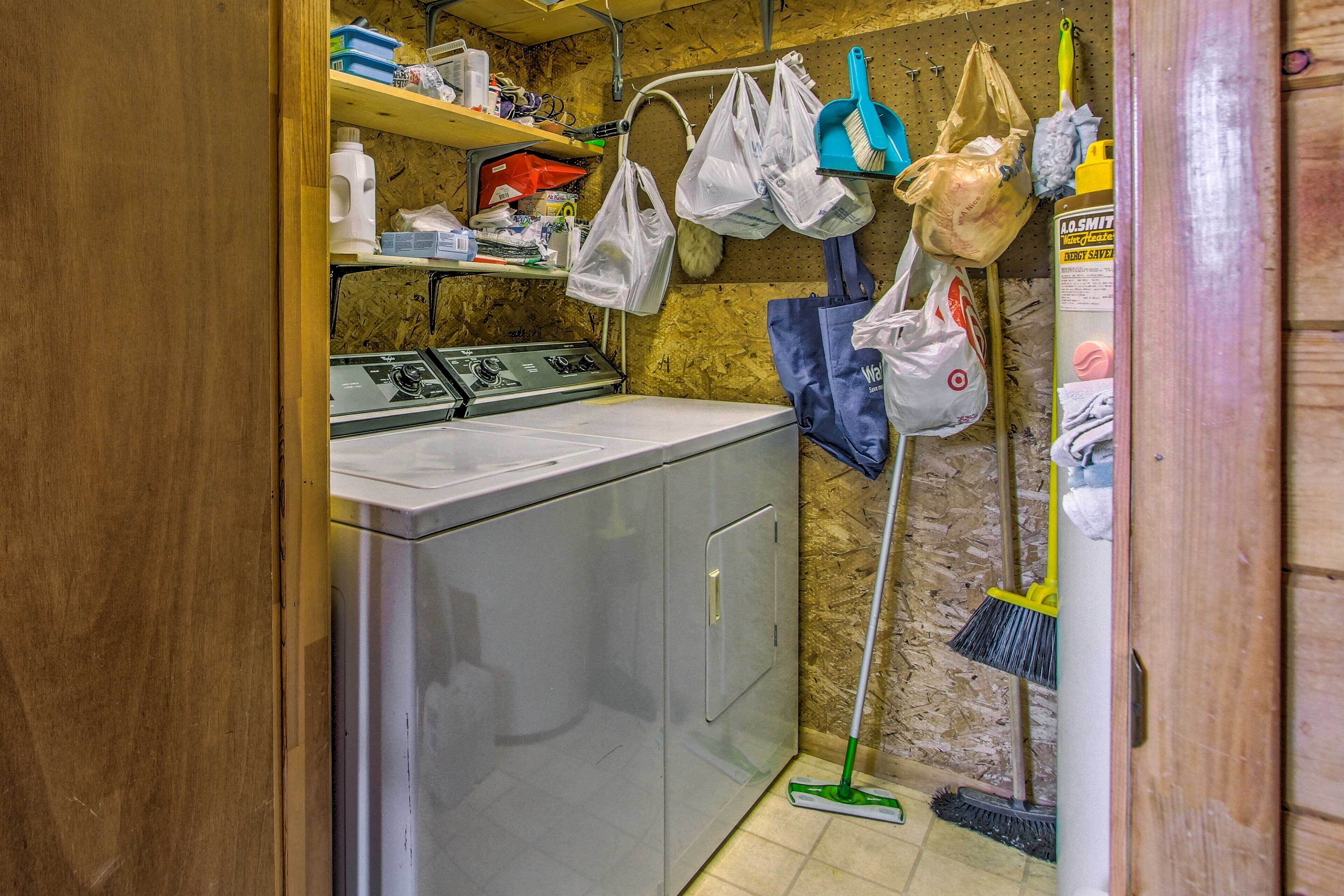 A laundry room with a washing machine, shelves with cleaning supplies, and a broom leaning against the wall.
