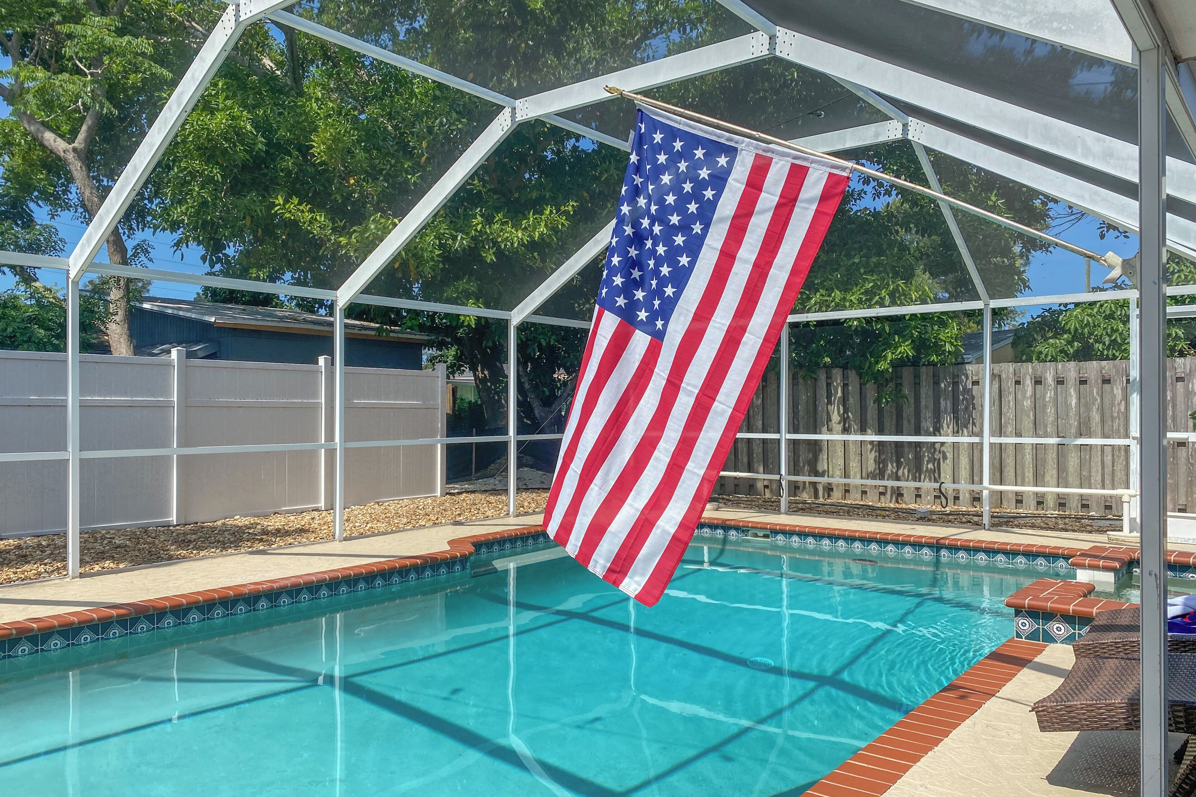 Une piscine dotée d’un espace couvert, d’une clôture en bois et d’un drapeau américain.