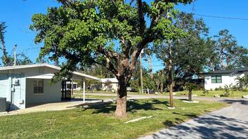 Un barrio residencial con un gran árbol en primer plano, una casa con porche cubierto y un cielo azul despejado.
