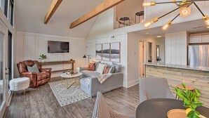 A spacious living area with a high ceiling, wooden beams, a grey sofa, a brown leather chair, and a dining table with a plant. - Designer Retreat w/ Pool, Golf + Beach Access! (Salem)