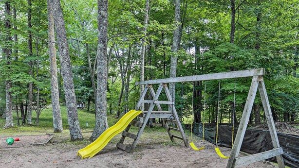 A wooden swing set with a yellow slide in a forested area. - Rustic Hayward Cabin With Spider Lake Access! (Hayward)