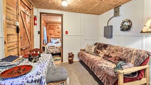 A cozy cabin-style room with a wooden ceiling, a couch, a table with a plaid tablecloth, and a teddy bear. - Rustic Hayward Cabin With Spider Lake Access! (Hayward)