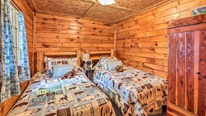 A cabin-style room with two beds, wooden walls, a ceiling fan, and a window with curtains. - Rustic Hayward Cabin With Spider Lake Access! (Hayward)