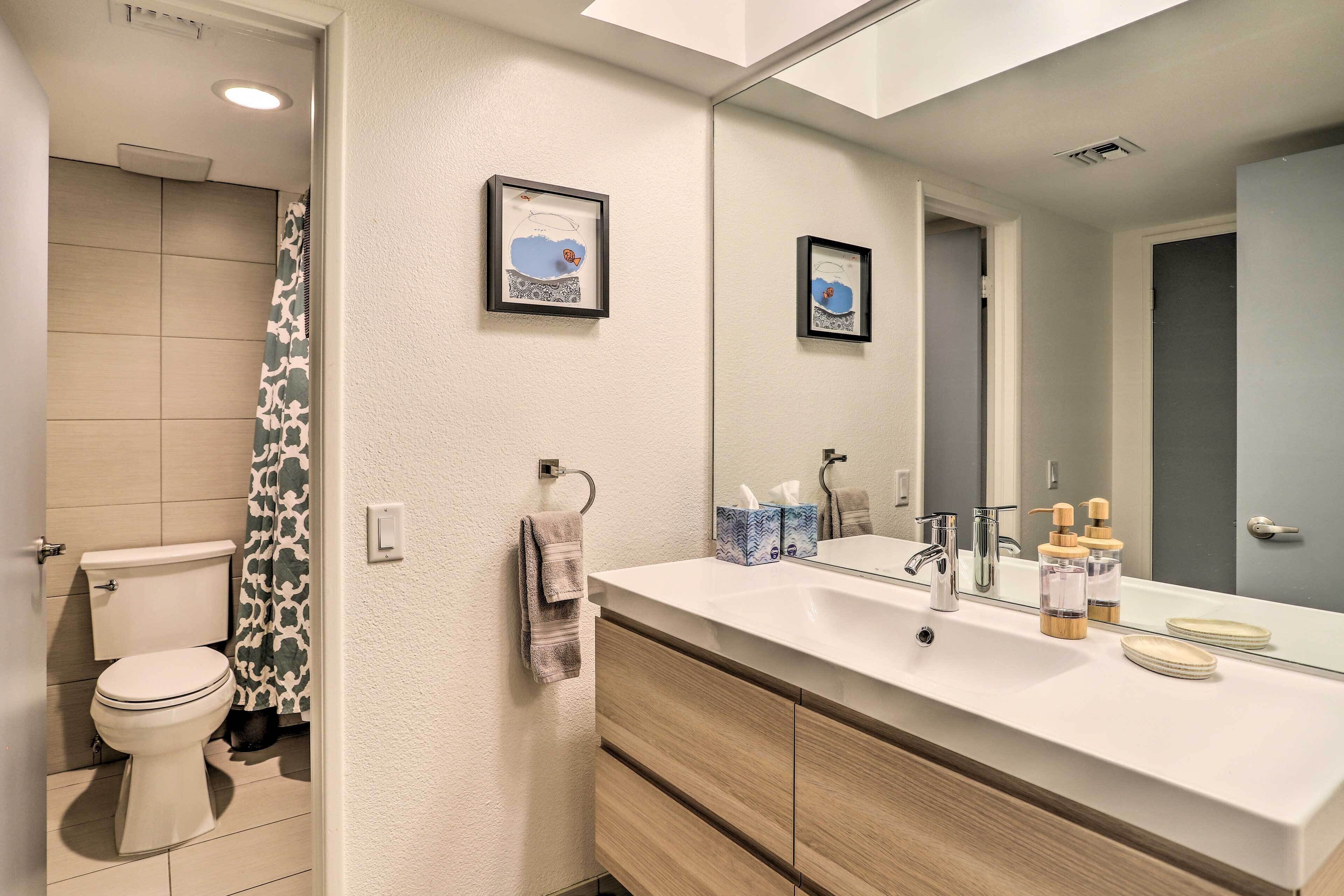A modern bathroom with a toilet, shower, vanity with a mirror, and a sink.