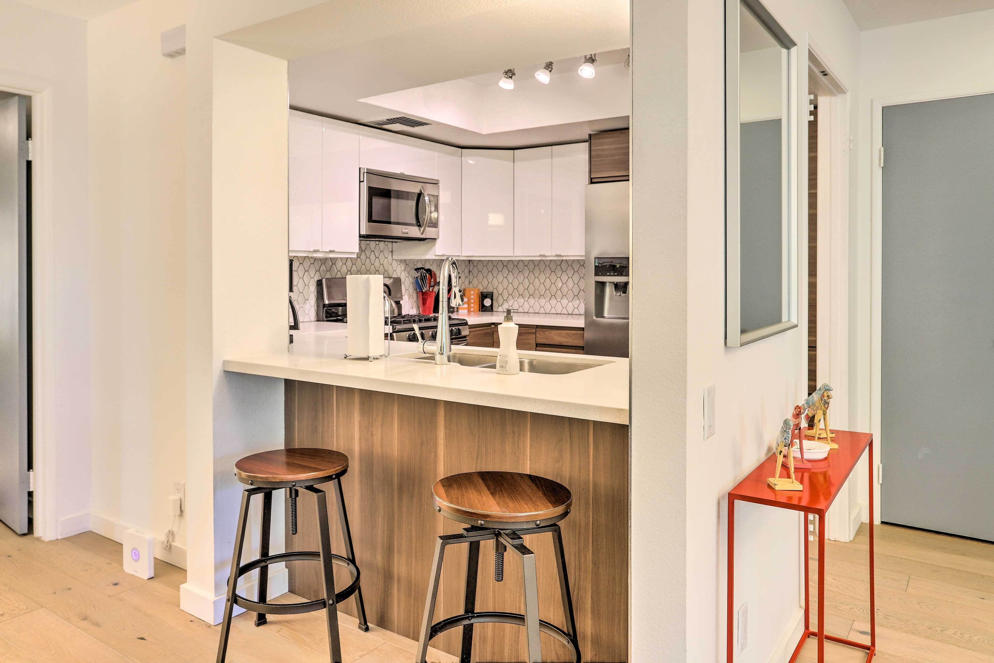 A modern kitchen with white cabinets, stainless steel appliances, and a wooden island with stools.