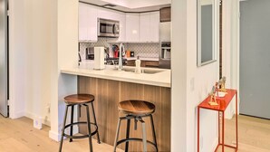 A modern kitchen with white cabinets, stainless steel appliances, and a wooden island with stools. - Palm Springs Hideaway w/ Resort Amenities! (Palm Springs)