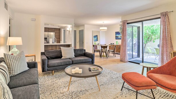 A modern living room with a grey sofa, a round coffee table, and a red armchair. There is a dining area with a table and chairs visible in the background. - Palm Springs Hideaway w/ Resort Amenities! (Palm Springs)