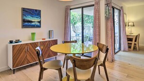 A dining area with a round table, wooden chairs, a cabinet with a geometric pattern, a painting on the wall, and patterned curtains. - Palm Springs Hideaway w/ Resort Amenities! (Palm Springs)