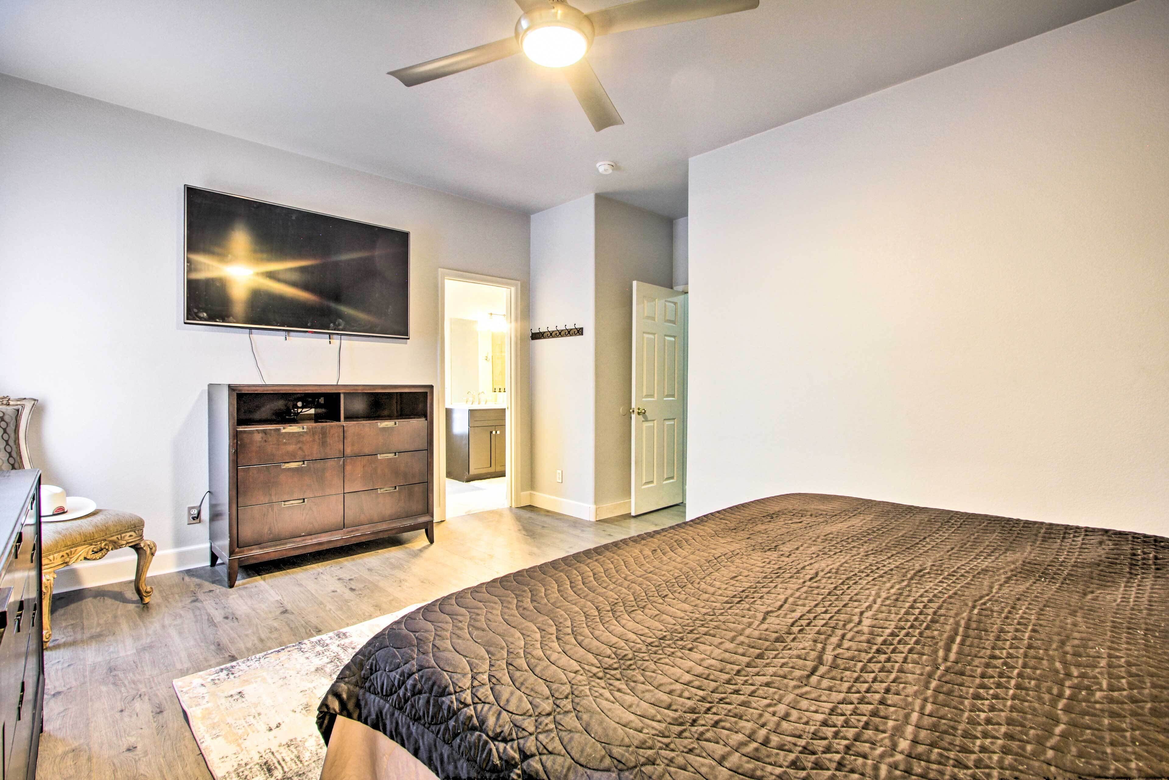 A bedroom with a large bed, a dresser, a television on the wall, and a ceiling fan.