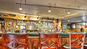 Eine Bar mit Holzhockern und einer Auswahl an Flaschen und Gläsern in Regalen.