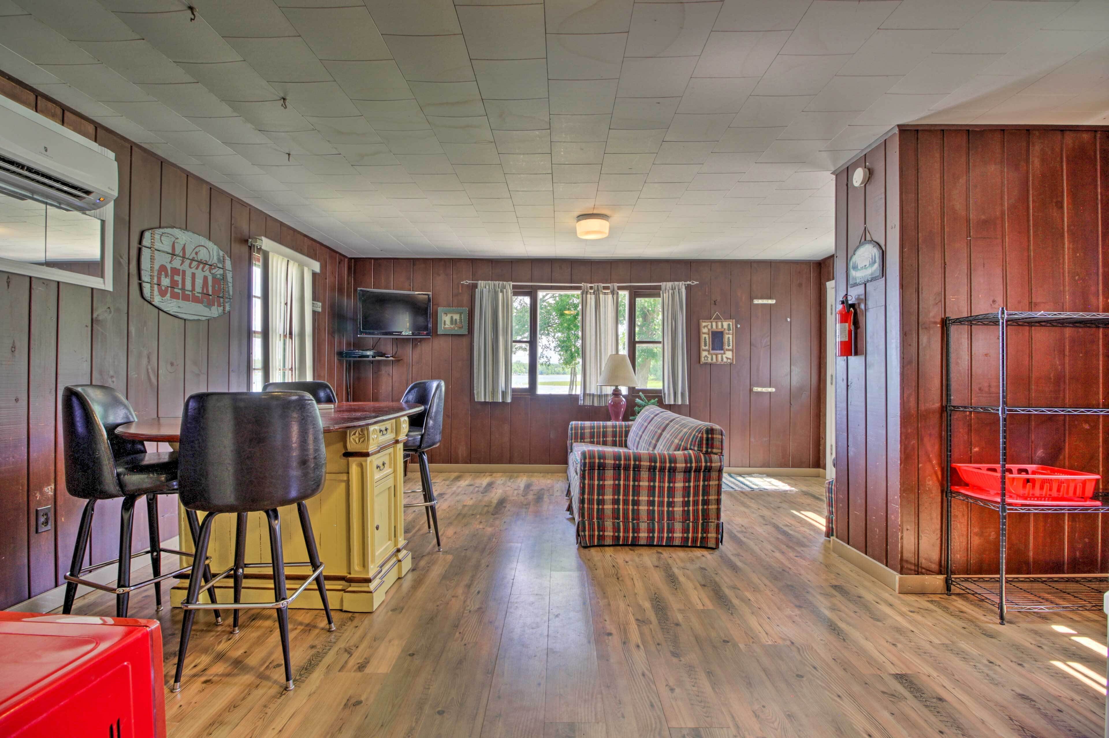A room with wooden walls, a bar area with stools, a sofa, a television, and a red storage unit.