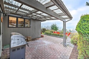 Un patio cubierto con una parrilla, vista al mar y un jardín bien cuidado.