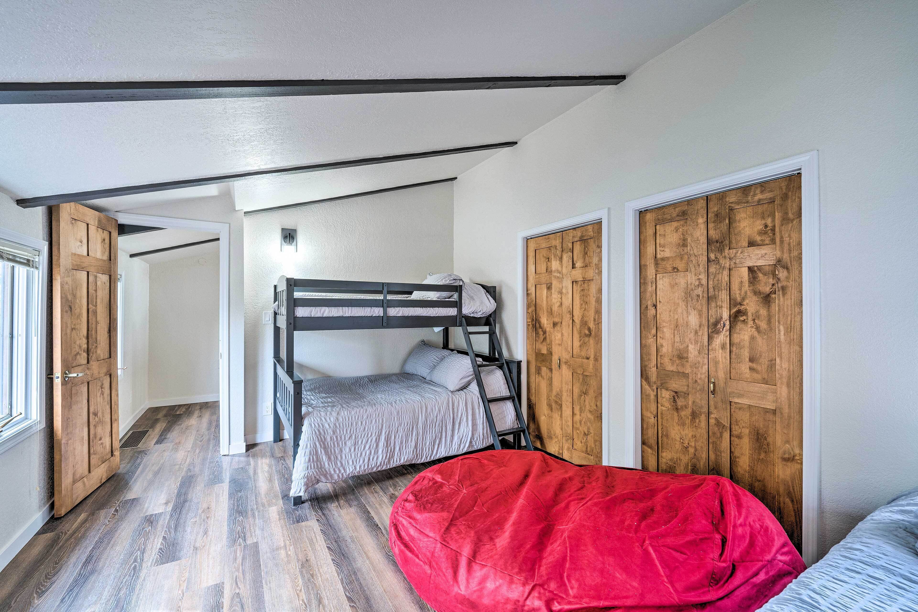 Una habitación con una litera, un sillón de orejas rojo, puertas de madera y un suelo con motivo de espiga.