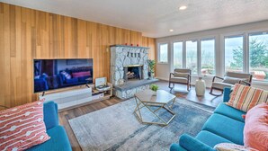 A modern living room with a stone fireplace, a large flat-screen TV, and a cozy seating area with blue sofas and a coffee table. - Lovely Coupeville Home w/ Puget Sound Views! (Coupeville)