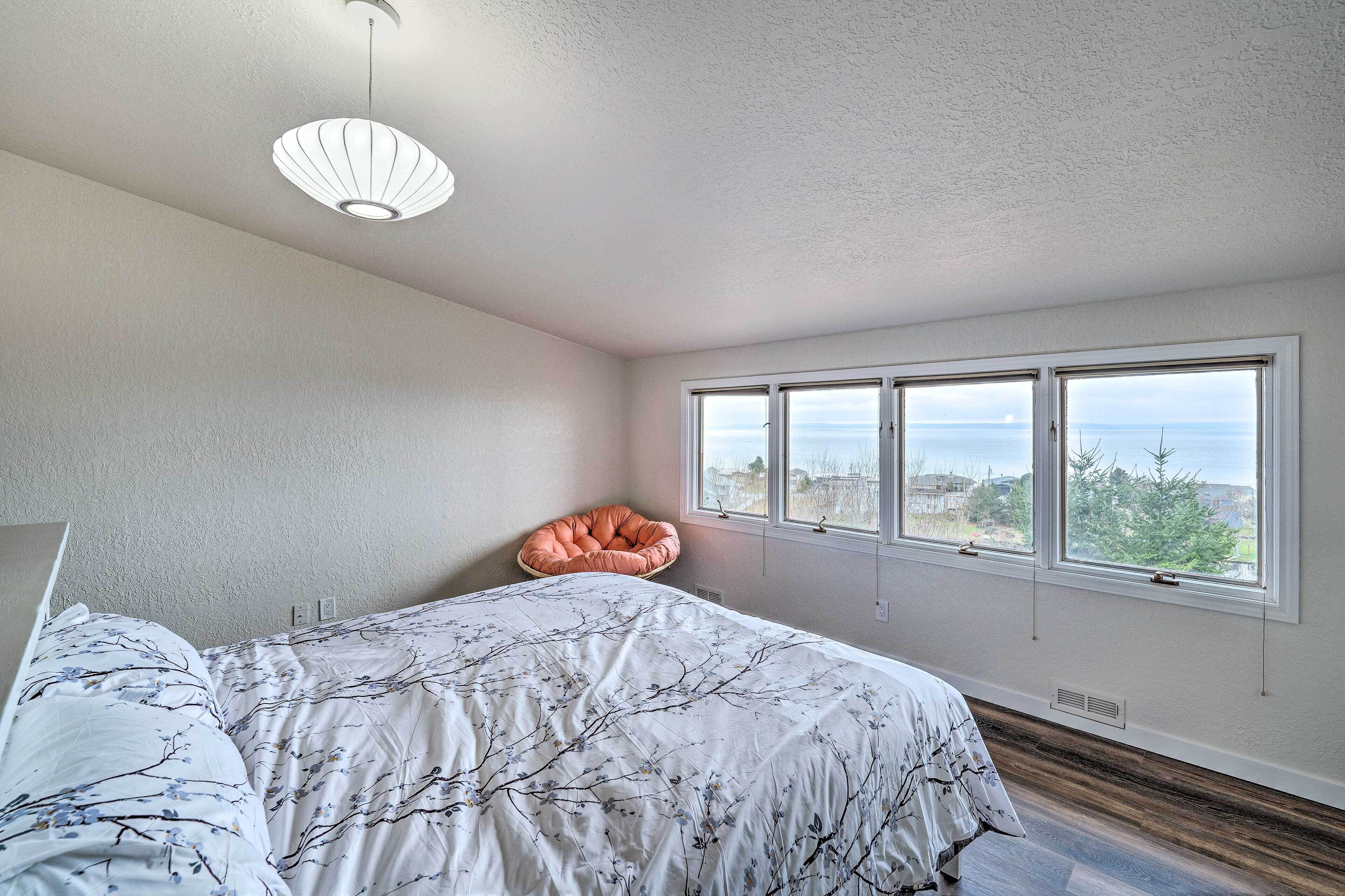 Un dormitorio con una cama grande, una ventana con vista al océano y una lámpara en el techo.