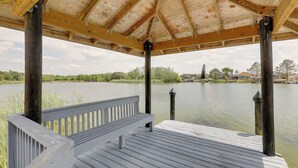 Un gazebo in legno con una panchina, affacciato su un lago tranquillo e una riva distante.