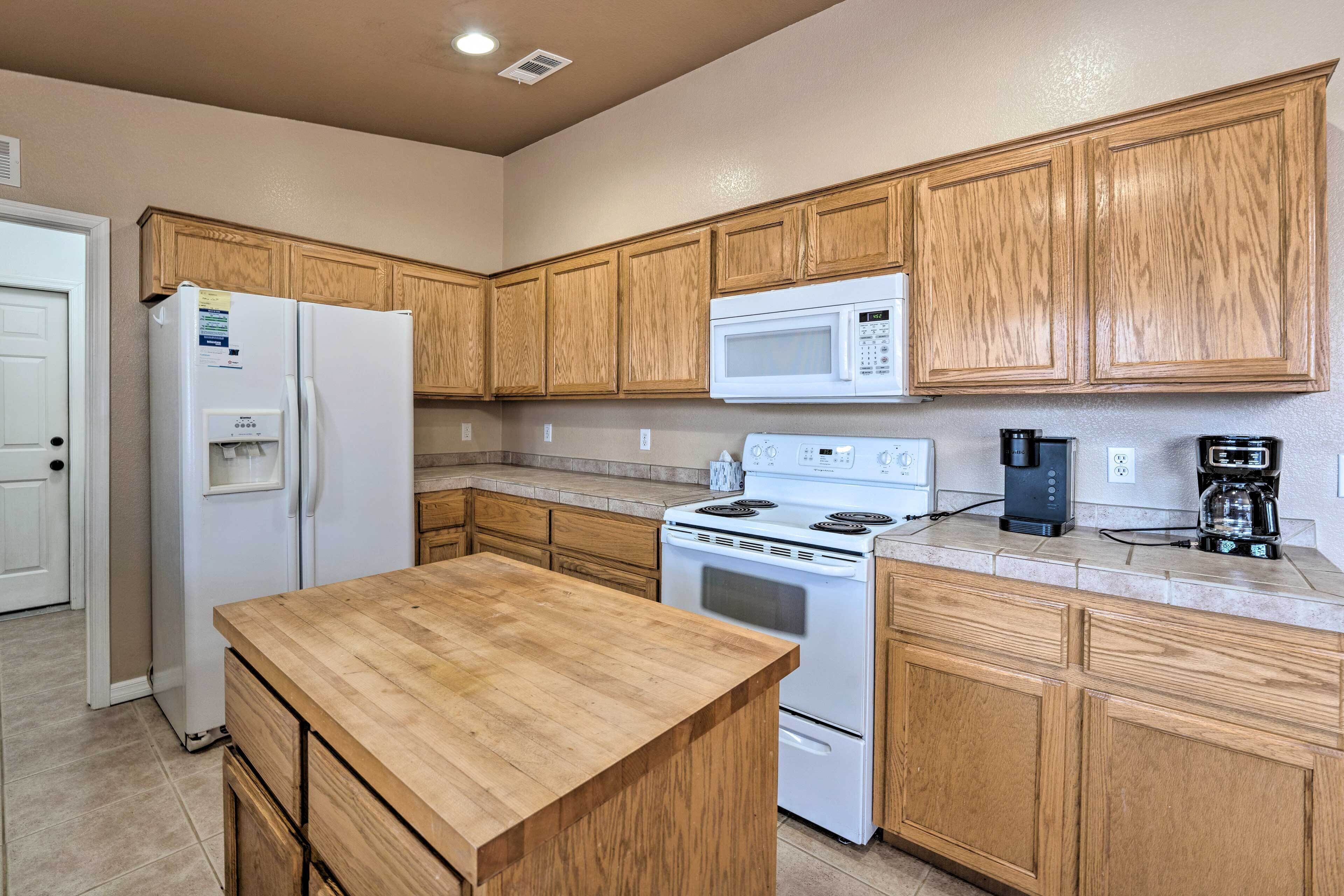 A kitchen with wooden cabinets, a white refrigerator, a microwave, a stove, and a coffee maker.