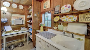 Een keuken met houten kastjes, een magnetron, een spoelbak en diverse decoratieve borden en kommen.