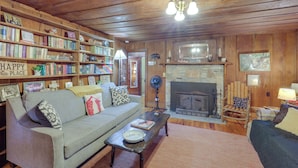 Een knus cabin interieur met een open haard, houten boekenkasten, een bank en een salontafel.