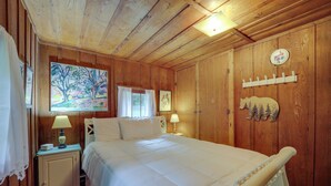 Een slaapkamer met houten lambrisering, een bed, nachtkastje, lamp, schilderij en een kapstok aan de muur.