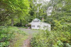 A white house with a green roof surrounded by dense forest.