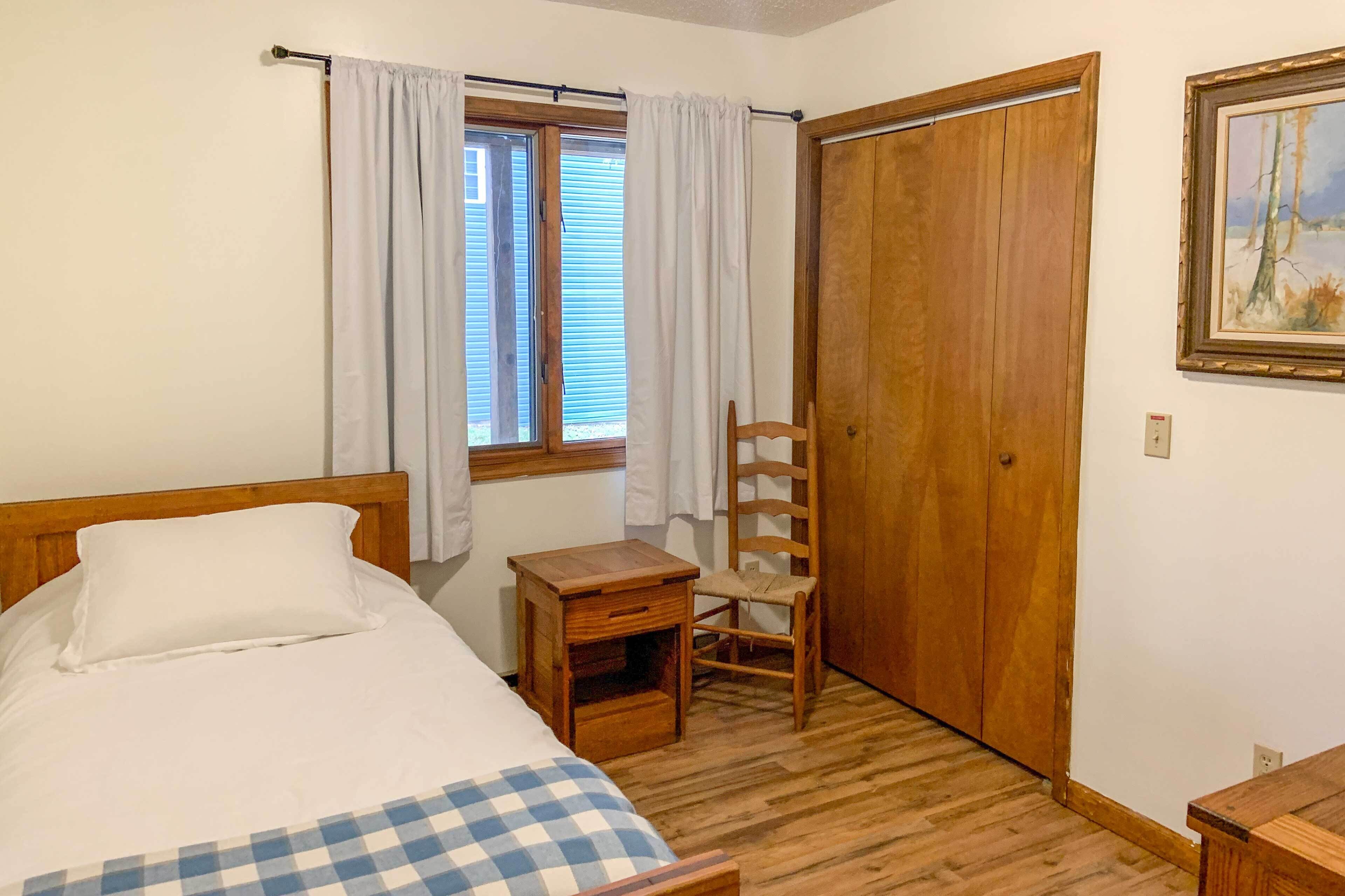Une chambre à coucher avec un lit, une table de chevet en bois, une chaise, une fenêtre avec des rideaux et une porte.