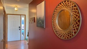 A hallway with a wooden floor, a white door, a framed picture, and a decorative mirror on a red wall. - 'the Overlook' in Massanuttens All Season Resort (McGaheysville)