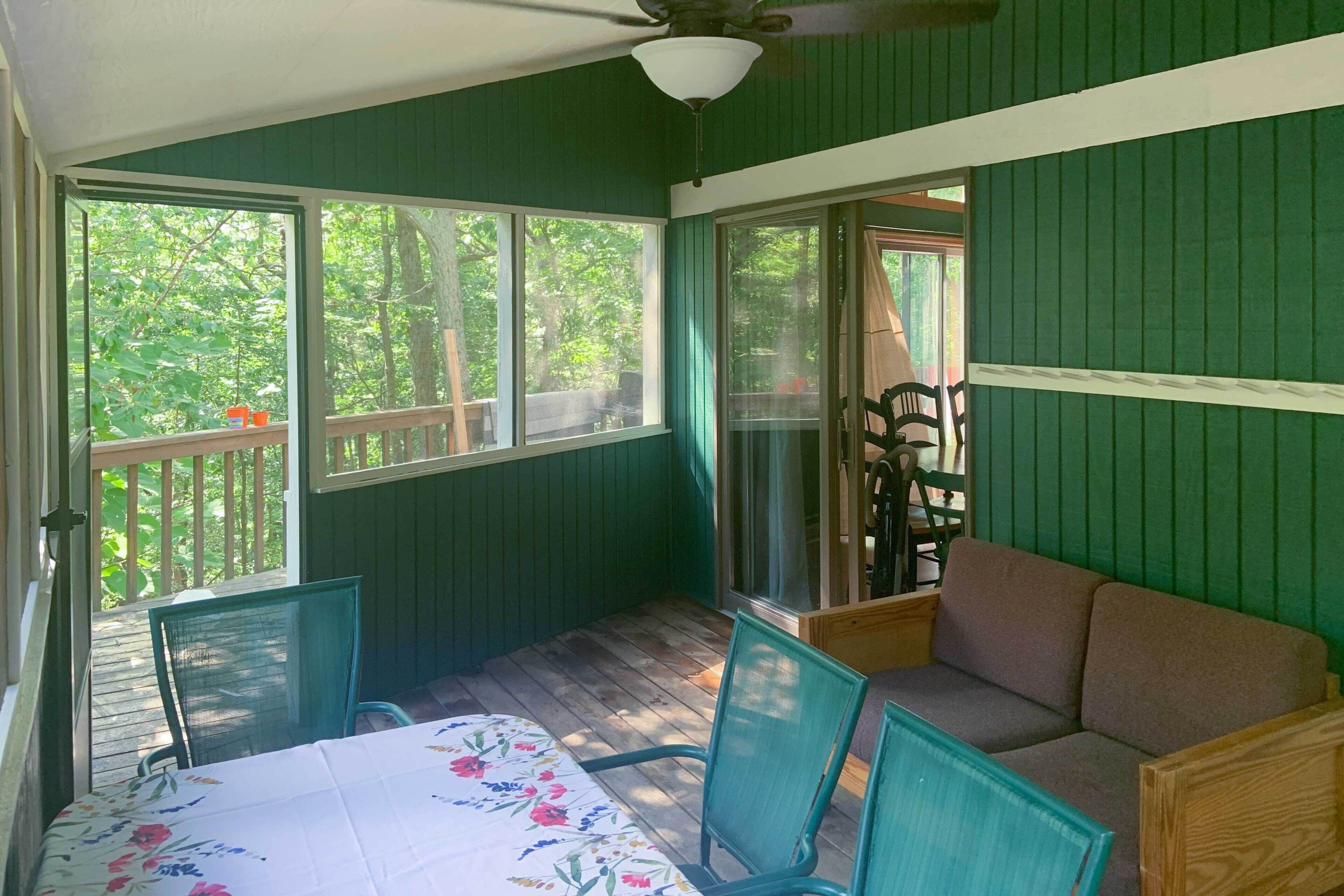 A covered patio with a table and chairs, a sofa, and large windows offering a view of the outdoors.