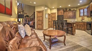 A spacious living room with a leather couch, a wooden coffee table, and a dining area with a kitchen in the background.