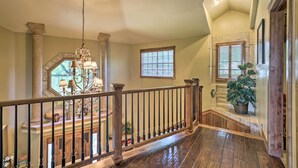 A spacious hallway with a wooden railing, a chandelier, and a potted plant.