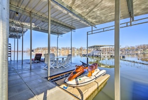 A jet ski on a dock, a covered seating area with chairs, and a view of a marina with boats. - Bayview Lake House w/ Dock on Lake of the Ozarks (Lake Ozark)