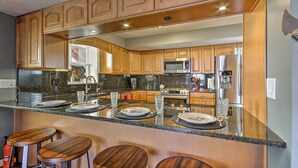 Una cocina con armarios de madera, encimera de granito y refrigerador de acero inoxidable.