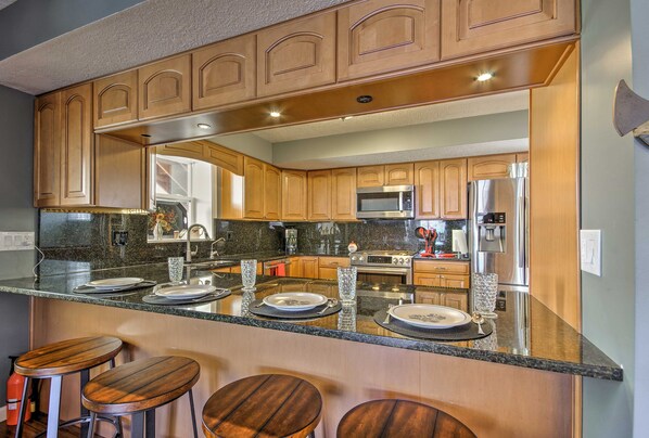 A kitchen with wooden cabinets, a granite countertop, and a stainless steel refrigerator. - Bayview Lake House w/ Dock on Lake of the Ozarks (Lake Ozark)