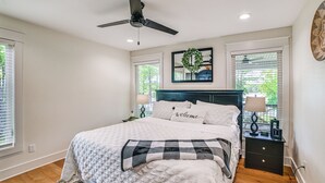 Een slaapkamer met een bed, een plafondventilator, een nachtkastje, een lamp en een raam met jaloezieën.