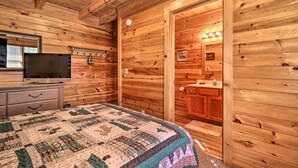 Une chambre à coucher située dans une cabane en bois, avec un lit, une commode, une télévision et une salle de bain visible à travers une porte ouverte.