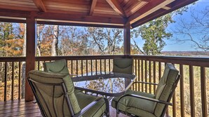 Un espace extérieur abrité, avec une table en verre et quatre chaises, offrant une vue sur un paysage boisé.