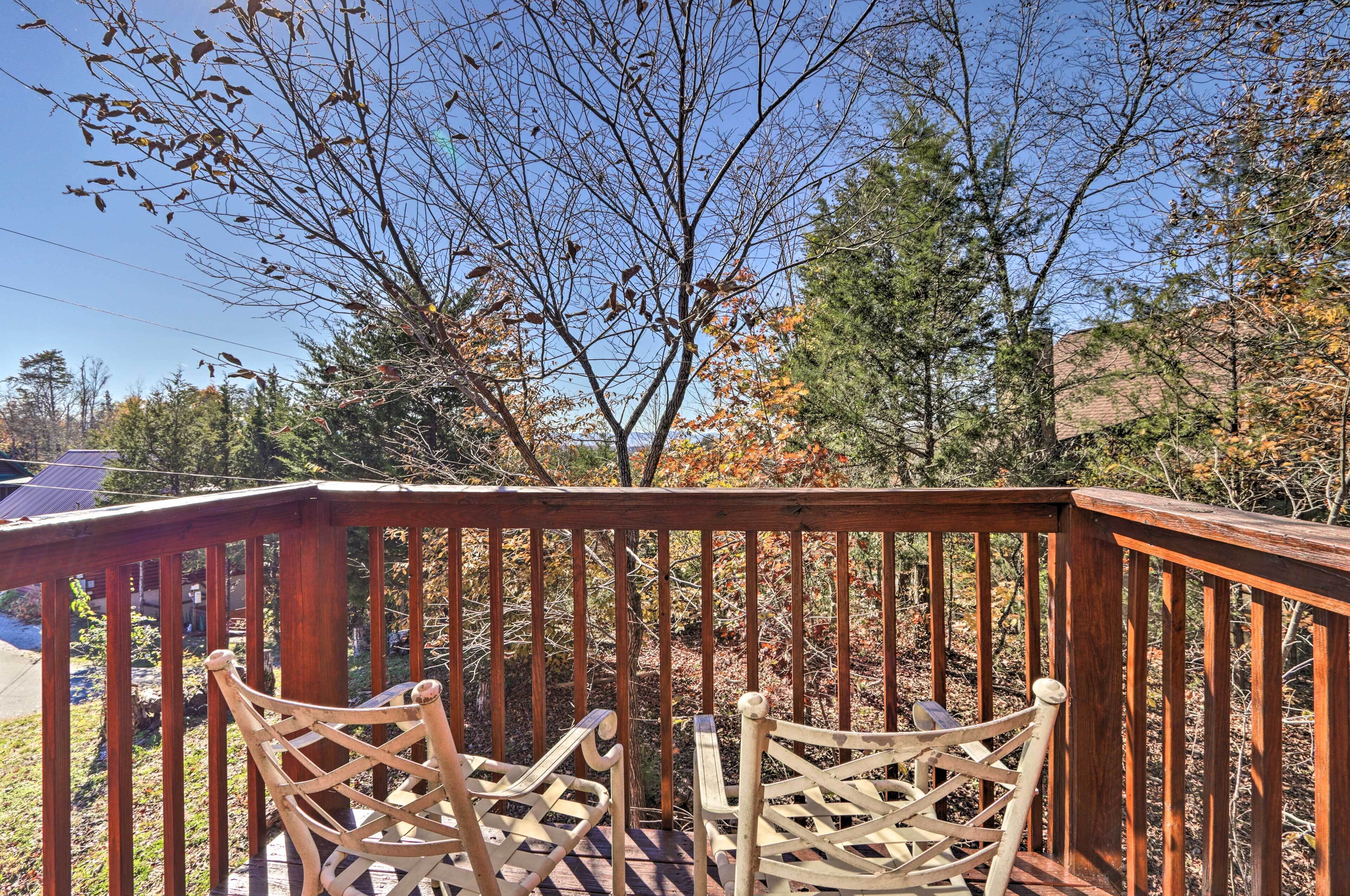 A wooden deck with four chairs facing a forested area.