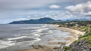 A coastal landscape with a sandy beach, waves, and a forested hill in the background. - Luxurious Newport Estate w/ Spa & Lighthouse Views (Newport)