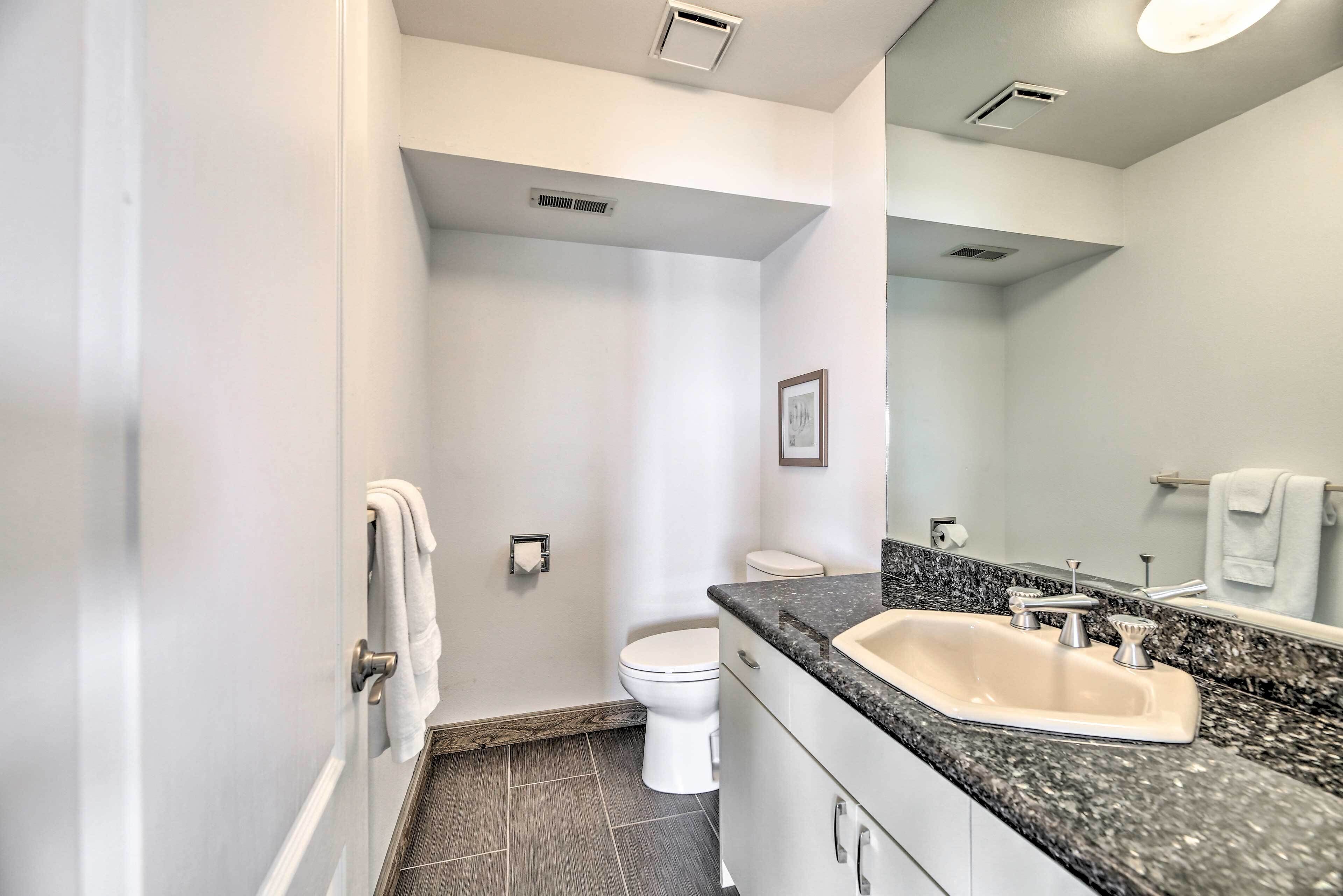 A modern bathroom with a white toilet, a sink with a granite countertop, and a mirror.