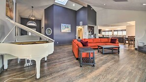A spacious living room with a grand piano, a vibrant orange sofa, and a wooden coffee table. - Luxurious Newport Estate w/ Spa & Lighthouse Views (Newport)
