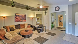 A living room with a sectional sofa, a coffee table, a side table, and a ceiling fan. There is a painting on the wall and a clock on the wall. - Charming Anthem Home w/ Fire Pit, 1 Mi to Park! (Phoenix)
