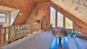 A cozy log cabin interior with a sloped ceiling, a wooden bookshelf, a telescope, and a view of the outdoors.